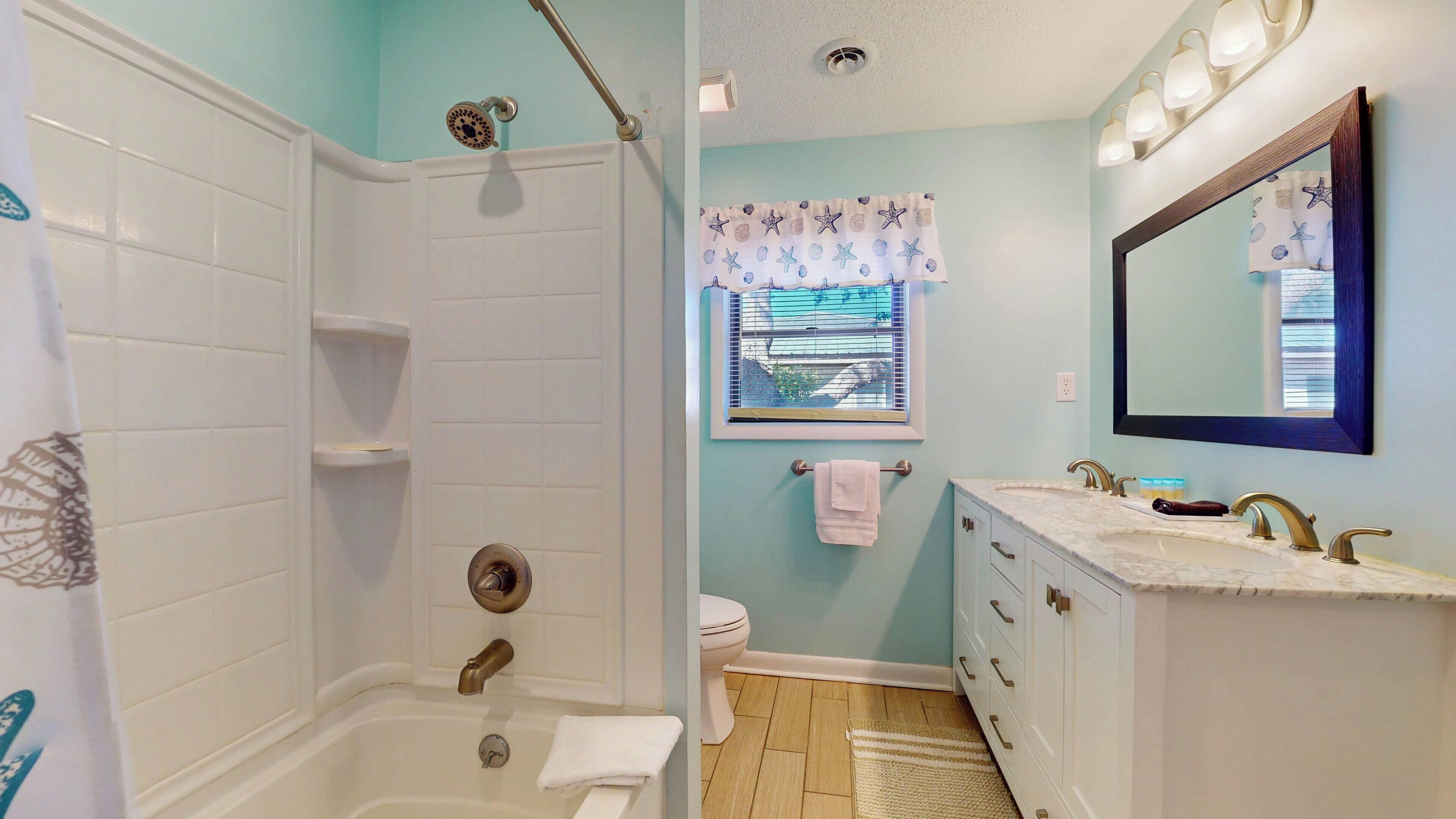 A bathroom with a bathtub, a shower, a toilet, a vanity with a mirror, and a window with a view of the outside.