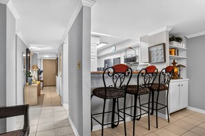 A modern kitchen with a bar area, white cabinetry, and a tiled floor.