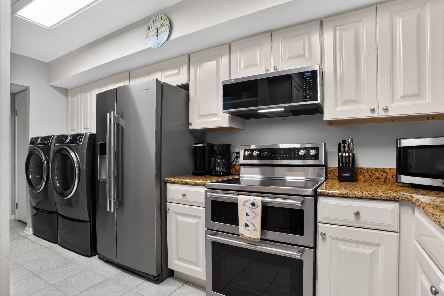 A modern kitchen with stainless steel appliances, white cabinetry, and a granite countertop.