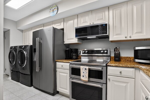 A modern kitchen with stainless steel appliances, white cabinetry, and a granite countertop.