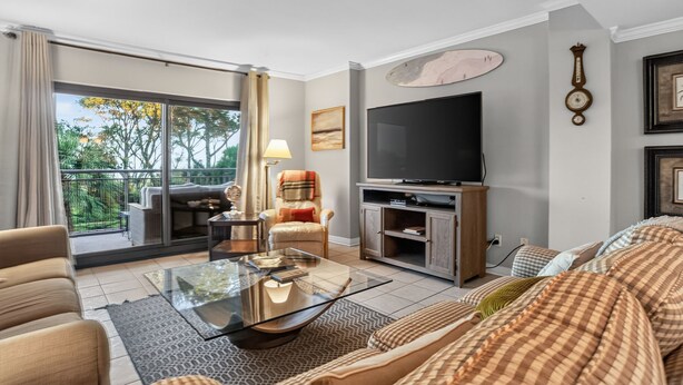 Een moderne woonkamer met een bank, een glazen salontafel, een televisie en een balkon met tuinmeubilair.