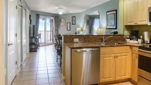 Una cocina con lavavajillas, encimera de granito, armarios de madera y vistas a un balcón.