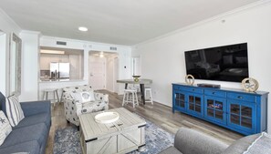 A living room with a sofa, coffee table, TV, and a blue cabinet. - Brightly colored beachfront condo w/private balcony! 🏖️ (Destin)