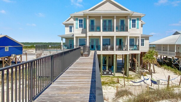 Una casa fronte spiaggia su due piani, con un balcone, un pontile in legno e una spiaggia sabbiosa.