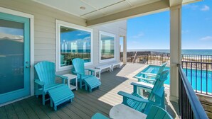 Un'area esterna coperta con piscina, poltrone Adirondack color turchese e vista sull'oceano.
