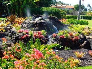 Um jardim com um elemento de água, rodeado por plantas coloridas.