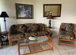 A living room with a floral sofa, a glass coffee table, a side table with a lamp, and a chair.