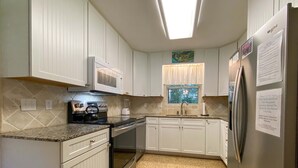 A kitchen with white cabinets, a stainless steel refrigerator, a microwave, and a window with a view of trees.