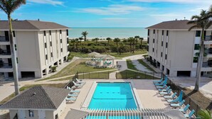 A hotel pool area with a view of the ocean, surrounded by palm trees and a gazebo. - Sanddollar #A202 is a 3/2 beachfront Vacation Rental on Sanibel Island (Sanibel)
