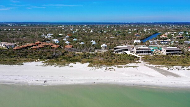 An aerial view of a coastal area with a beach, a river, and several buildings including a hotel with multiple floors and a pool. - Sanddollar #A202 is a 3/2 beachfront Vacation Rental on Sanibel Island (Sanibel)