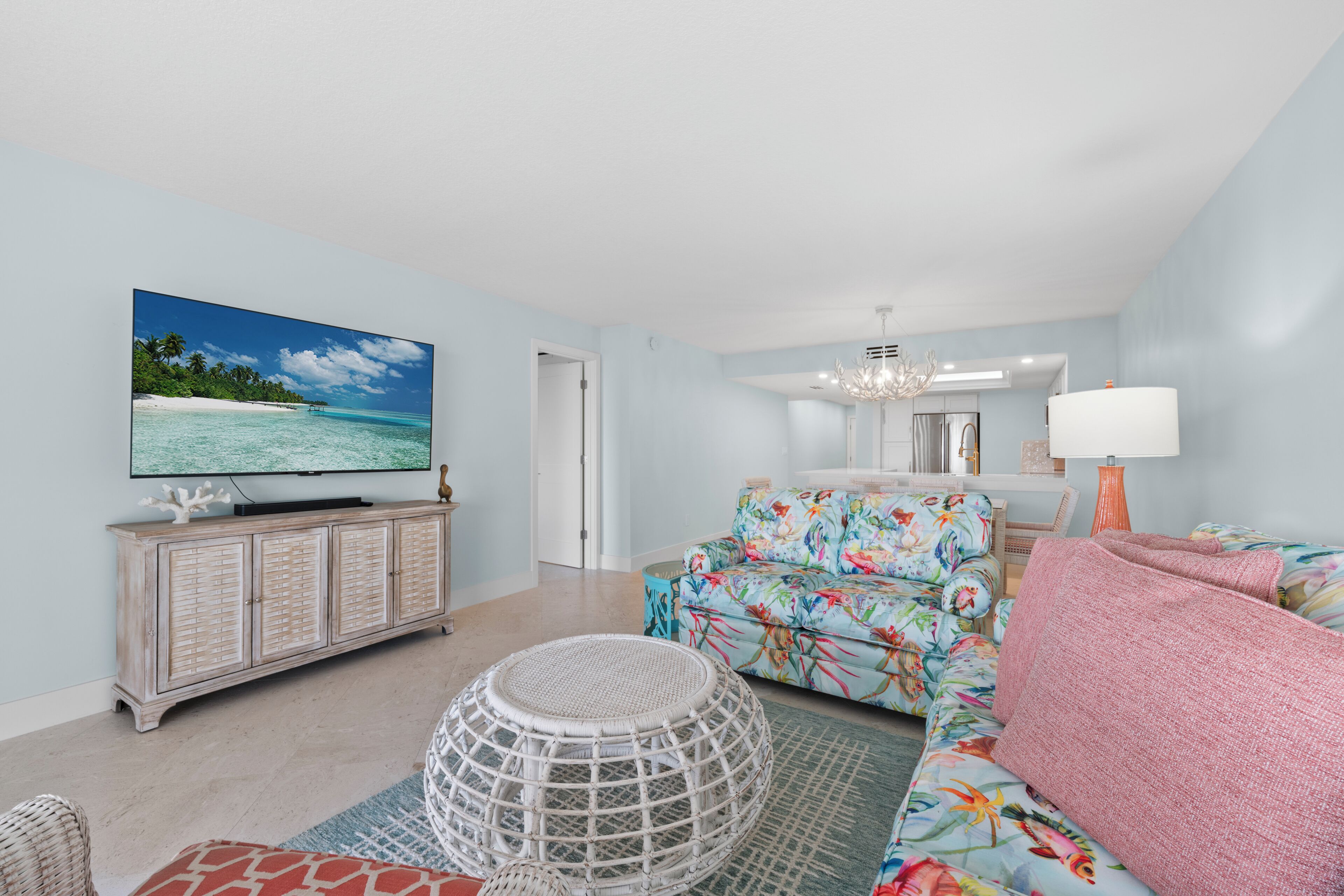A living room with a television, a sofa, a coffee table, and a dining area with a chandelier.