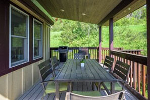Una terraza cubierta al aire libre con mesa y sillas de madera, una parrilla y un banco.