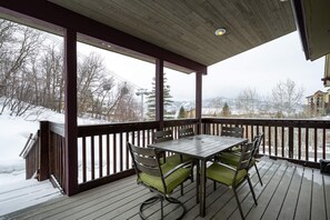 Una terraza techada al aire libre con una mesa y sillas de madera, barandilla y vistas a un paisaje nevado.