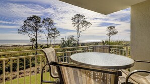 A balcony with a round table and chairs, overlooking a beach and trees.