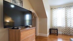 A modern living room with a flat-screen TV on a wooden cabinet, a small table, and a window with chevron-patterned curtains. - Salem 3rd floor 3BR Apartment (Salem)