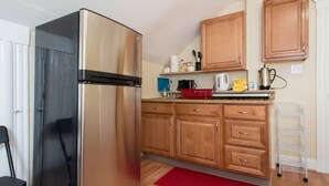 A compact kitchen with wooden cabinets, a stainless steel refrigerator, a red rug, and a metal drying rack. - Salem 3rd floor 3BR Apartment (Salem)