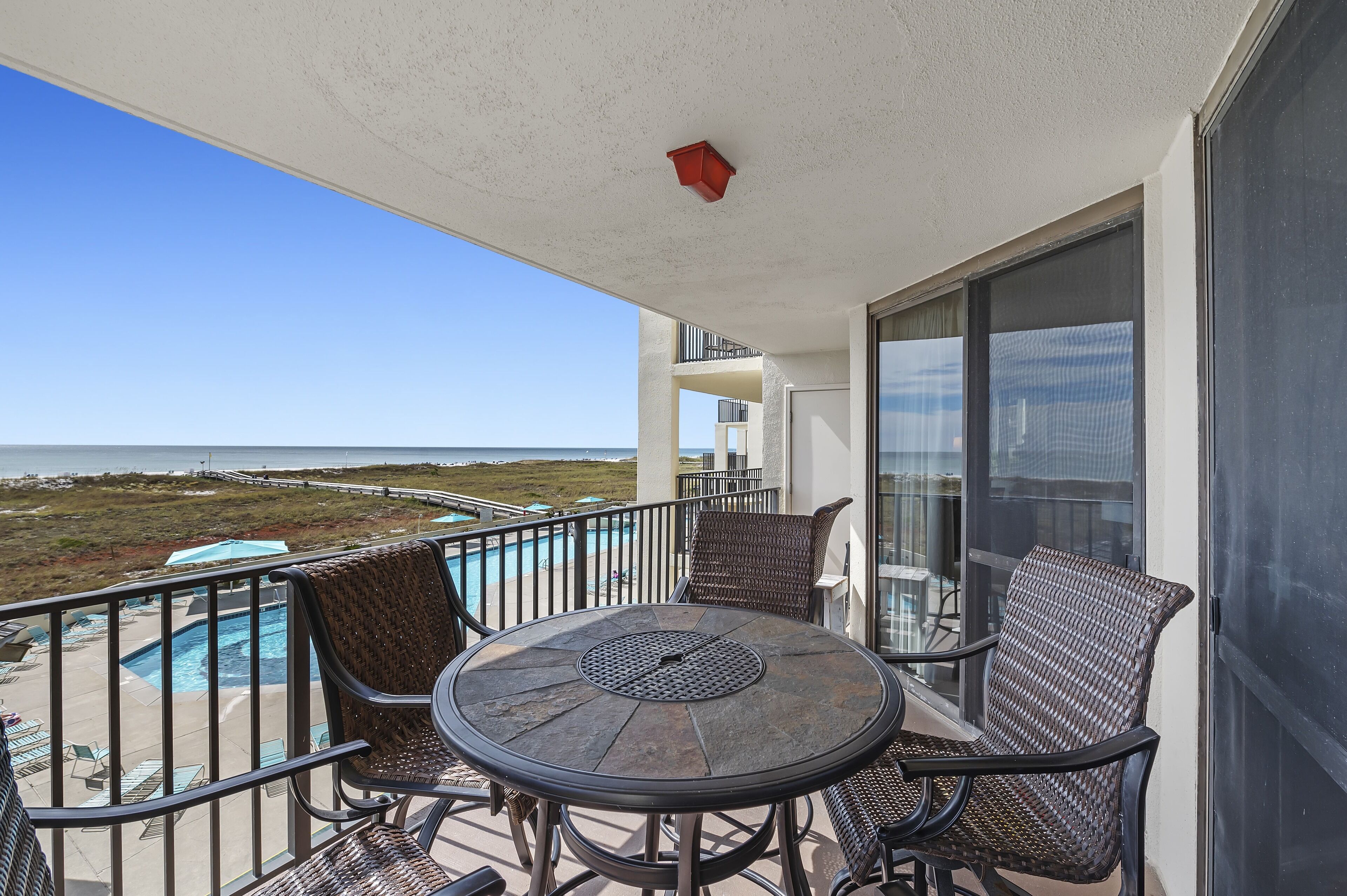 A balcony with a pool, wicker chairs, and a table.