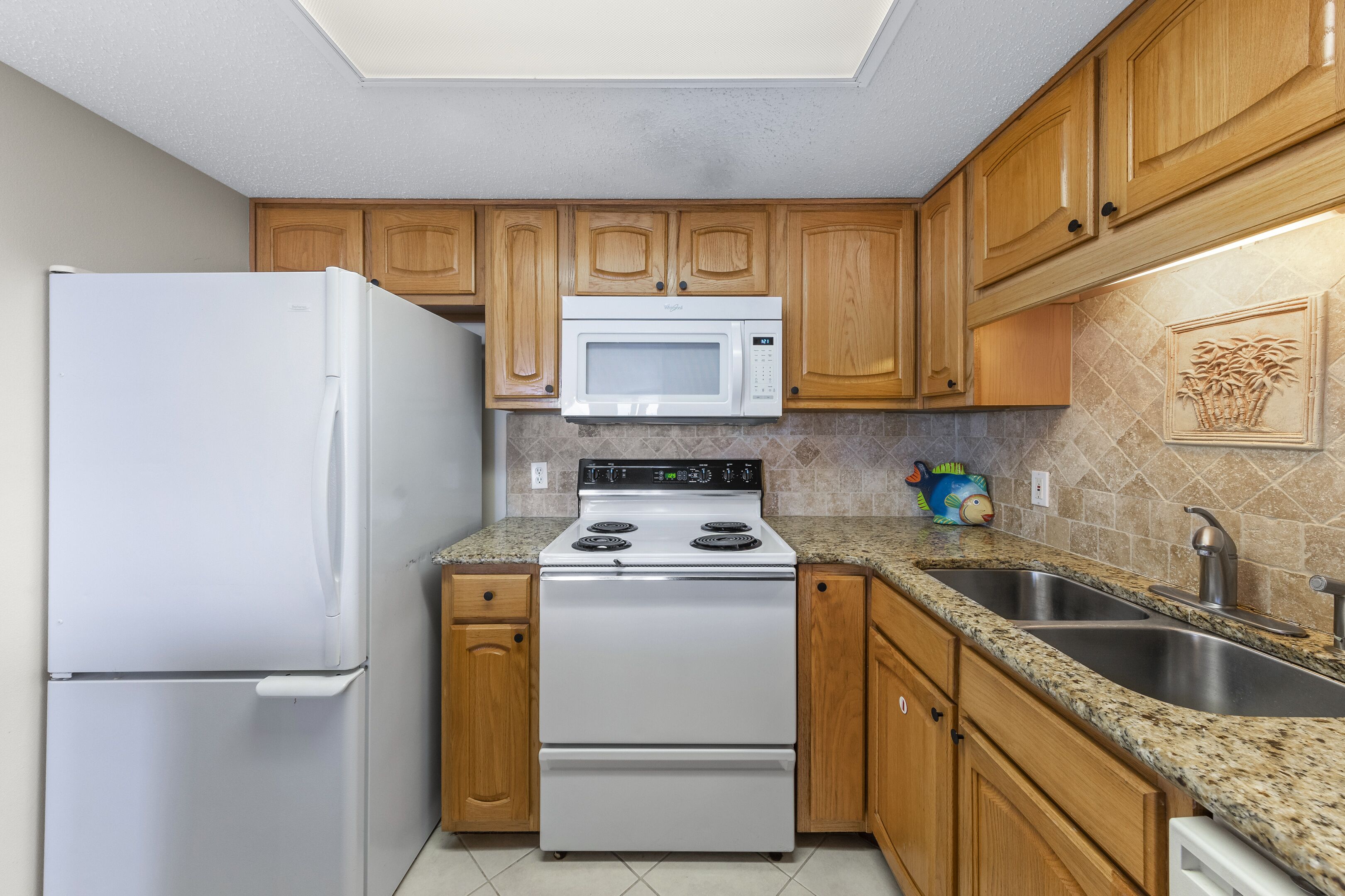A kitchen with wooden cabinets, a white refrigerator, a microwave, a stove, and a granite countertop.