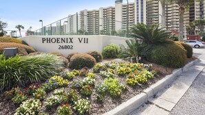 A landscaped area with a sign reading "PHOENIX VII 26802" and a row of colorful flowers. - Phoenix VII 213 | Beachfront | Pools | Fitness Center | My Beach Getaways (Orange Beach)