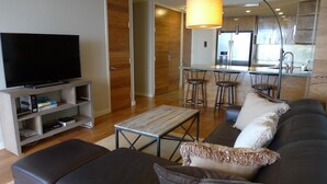 Een moderne woonkamer met een flatscreen televisie, een bank, een salontafel en een keuken in de achtergrond.