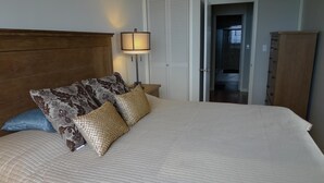 Een net opgemaakt bed met gestreepte kussens, een houten hoofdbord, een bedlampje en een garderobe in een slaapkamer.