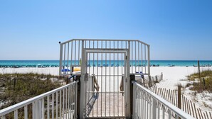 Ein Eingangstor zum Strand, der zu einem sandigen Strand mit Sonnenschirmen und Liegestühlen führt.