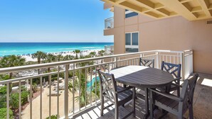 Ein Balkon mit Tisch und Stühlen, mit Blick auf einen Strand mit Sonnenschirmen und Palmen.