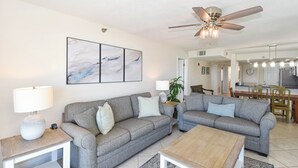 Ein Wohnzimmer mit zwei grauen Sofas, einem Holztisch, einem Deckenventilator und abstrakter Wandkunst.