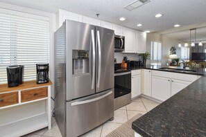 A modern kitchen with stainless steel appliances, white cabinetry, and a granite countertop. - Corner condo at Destin Towers overlooking Gulf-front pool & beach! (Destin)