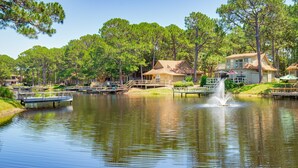 A lakeside resort with docked boats, a fountain, and cabins with outdoor seating.