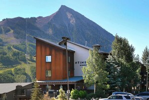 A building with a sign reading 'TIME 20 MARCH,' surrounded by trees and a mountain in the background. - The North Face, Hot tub, Timbers Condo, Shuttle (Mt. Crested Butte)