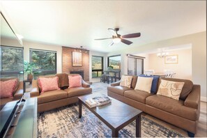 A spacious living room with leather sofas, a coffee table, and a ceiling fan.