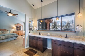 A modern bathroom with a large mirror, dual sinks, and a ceiling fan.