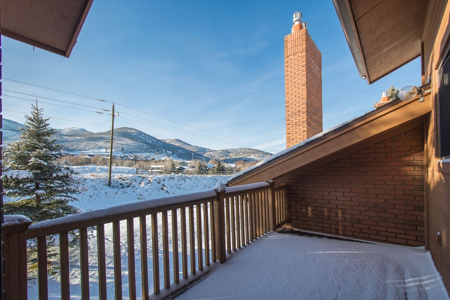 Un balcón con suelo cubierto de nieve, un edificio de ladrillo y una vista despejada de una cadena montañosa distante.