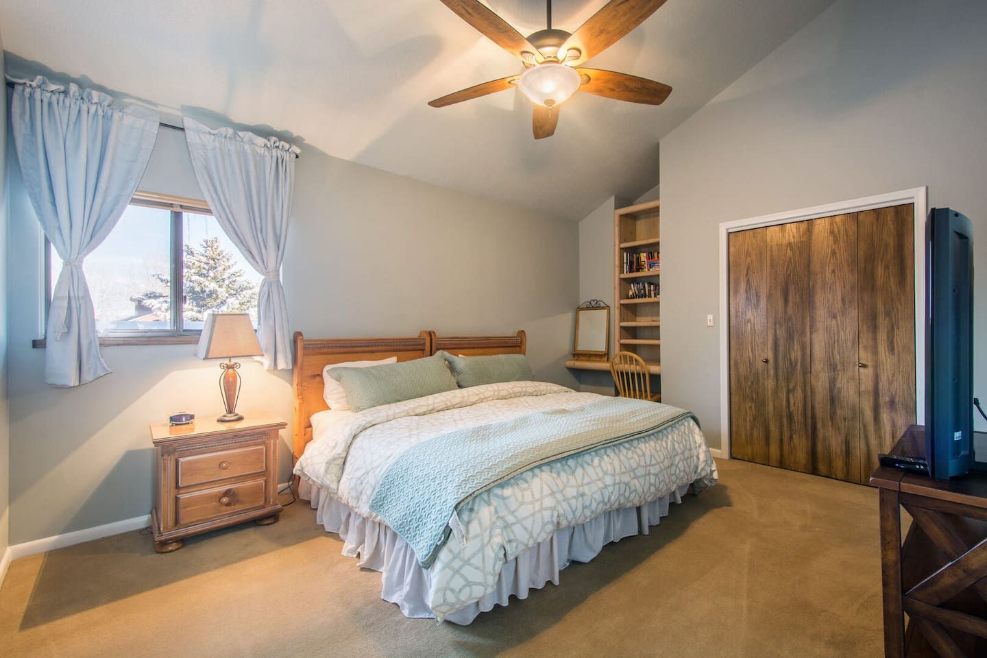 A bedroom with a bed, a nightstand, a lamp, a ceiling fan, a bookshelf, and a wardrobe.