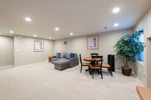 A spacious room with a grey sectional sofa, a dining table with chairs, and a potted plant.