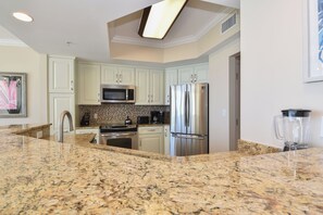 Cozinha com bancadas de granito, eletrodomésticos de aço inoxidável e armários em tons claros.