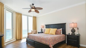 Un'ampia camera da letto con un grande letto, un ventilatore a soffitto e vista sull'oceano attraverso ampie finestre.