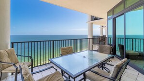 Un balcón con una mesa y sillas de vidrio, con vistas al mar azul y despejado.