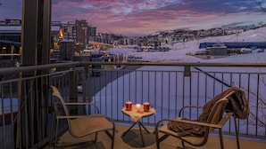 A balcony with two chairs, a table with two mugs and a candle, and a view of a snowy town with buildings and a ski lift. - Prime Views | One Steamboat Place 516 Wild Card (Steamboat Springs)