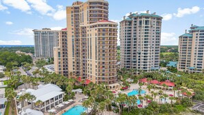 A high-rise hotel with multiple balconies, a swimming pool, and a landscaped area with palm trees. - Beachfront ~ Spacious Kitchen ~ Private Balcony (Miramar Beach)