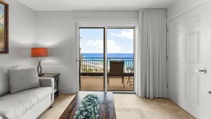 A room with a sofa, a table with a plant, a lamp, and a view of the sea through a sliding door. - Beachfront ~ Spacious Kitchen ~ Private Balcony (Miramar Beach)
