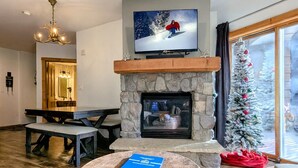 Una sala de estar acogedora con una chimenea de piedra, un televisor montado encima y un árbol de Navidad.