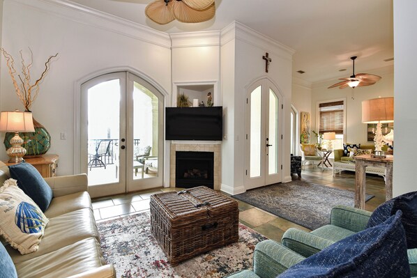 A living room with a fireplace, a television, and a large wicker chest. - Stylish Beach Home w/Private Elevator & Beach Access (Destin)