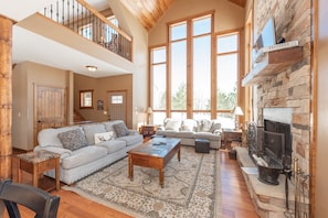 A spacious living room with a high ceiling, a fireplace, a large window, and a cozy seating area.