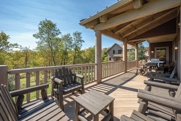 A wooden deck with seating and a covered area, overlooking a forested area.