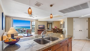 A modern kitchen with a large island, double sink, and a view of the ocean. - Maui Resort Rentals:  Honua Kai Konea 933 – 2 BR Corner w/ Sweeping 9th Floor Ocean and Black Rock Views! (Lahaina)