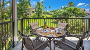 A balcony with a round table set for breakfast, surrounded by chairs, overlooking a lush garden and a clear blue sky. - Kahala 422 Poipu Tropical Nature By Suite Paradise (Koloa)