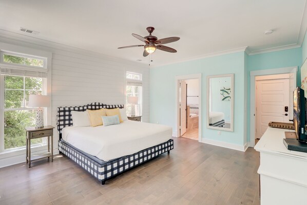 A bedroom with a large bed, a ceiling fan, and a view of the bathroom through an open door.