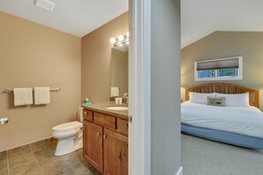 Une salle de bain avec des toilettes, un lavabo et un meuble-lavabo. On y trouve un lit avec une tête de lit et un oreiller orné d’un motif textuel.